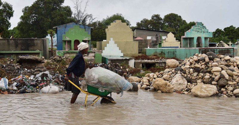 woman pushes wheelbarrow through flood waters in Haiti after Hurricane Matthew